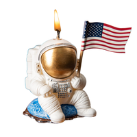 Southlake Gifts Astronaut Landing Candle lit featuring an astronaut holding a U.S. flag while seated on a blue planet in a white back ground.