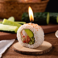 Southlake Gifts California Roll Sushi Candle burning on a wooden coaster, handmade lemon scented candle with realistic sushi details for foodie gifts.