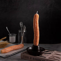 Southlake Gifts Churros Candle Set featuring two realistic churro-shaped taper candles, one standing upright in the handmade holder and one resting beside it on a marble table. Minimalist dark background adds a cozy café aesthetic, perfect for dessert lovers and handmade candle décor unique gifts