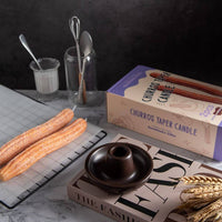 Southlake Gifts Churros Taper Candle Set featuring two churro-shaped candles in ceramic candle holder beside the packaging. A whimsical dessert candle design and thoughtful holiday gift idea for food lovers and home décor fans.