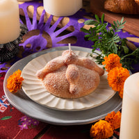 Handmade Pan de Muerto bread candle lit on altar with marigolds and papel picado, Southlake Gifts Día de los Muertos food candle decoration.