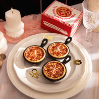 Southlake Gifts Heart Pepperoni Mini Pizza Candle Trio displayed on a decorative plate with its gift-ready packaging behind it, featuring three realistic mini pepperoni food candles in reusable skillets. A unique novelty candle set perfect for gifting and home décor.