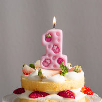 Lit pink strawberry number one candle from Southlake Gifts used as a birthday cake topper, sitting on a cupcake with realistic strawberry details, handmade decorative wax candle.