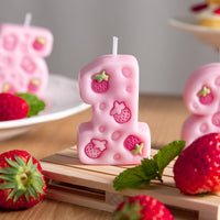 Close-up of pink strawberry number one candle with four engraved strawberries, cute birthday number candle cake topper décor.