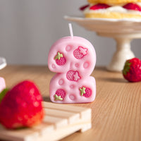 Close-up of pink strawberry number two candle with five engraved strawberries, cute birthday number candle cake topper décor.