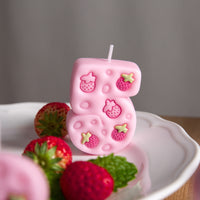 Close-up of pink strawberry number five candle with five engraved strawberries, cute birthday number candle cake topper décor.