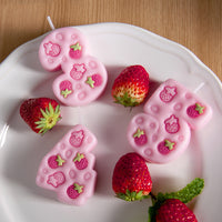 Close-up of pink strawberry number three, four, and five candles with five engraved strawberries, cute pink birthday number candle cake toppers displayed on a plate.