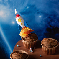 Southlake Gifts rocket launch candle lit on a cupcake as a space themed cake topper, handmade soy wax rocket with flame effect, a playful gift for space lovers and birthday celebrations.