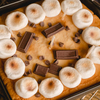 Macro detail of the Skillet S’mores Chocolate and Marshmallow Candle showing the cookie base, mini chocolate bars, chocolate chips, and toasted marshmallow toppings, a realistic handmade dessert candle designed to look like baked s’mores and a playful novelty candle gift for food lovers.