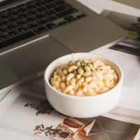 Southlake Gifts Macaroni & Cheese Pasta Candle in a white bowl placed beside a laptop — handmade butter cheese-scented food novelty candle designed like creamy mac and cheese, an artisan fun décor piece that makes a thoughtful candle gift.