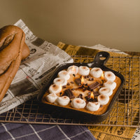 Skillet S'more chocolate cookie food candle from Southlake Gifts is lit on and sitting on a table as a unique table top food candle decor — handmade chocolate-scented candle with realistic marshmallow and cookie wax melts, a perfect cozy gift for smore dessert lovers and home décor fans.