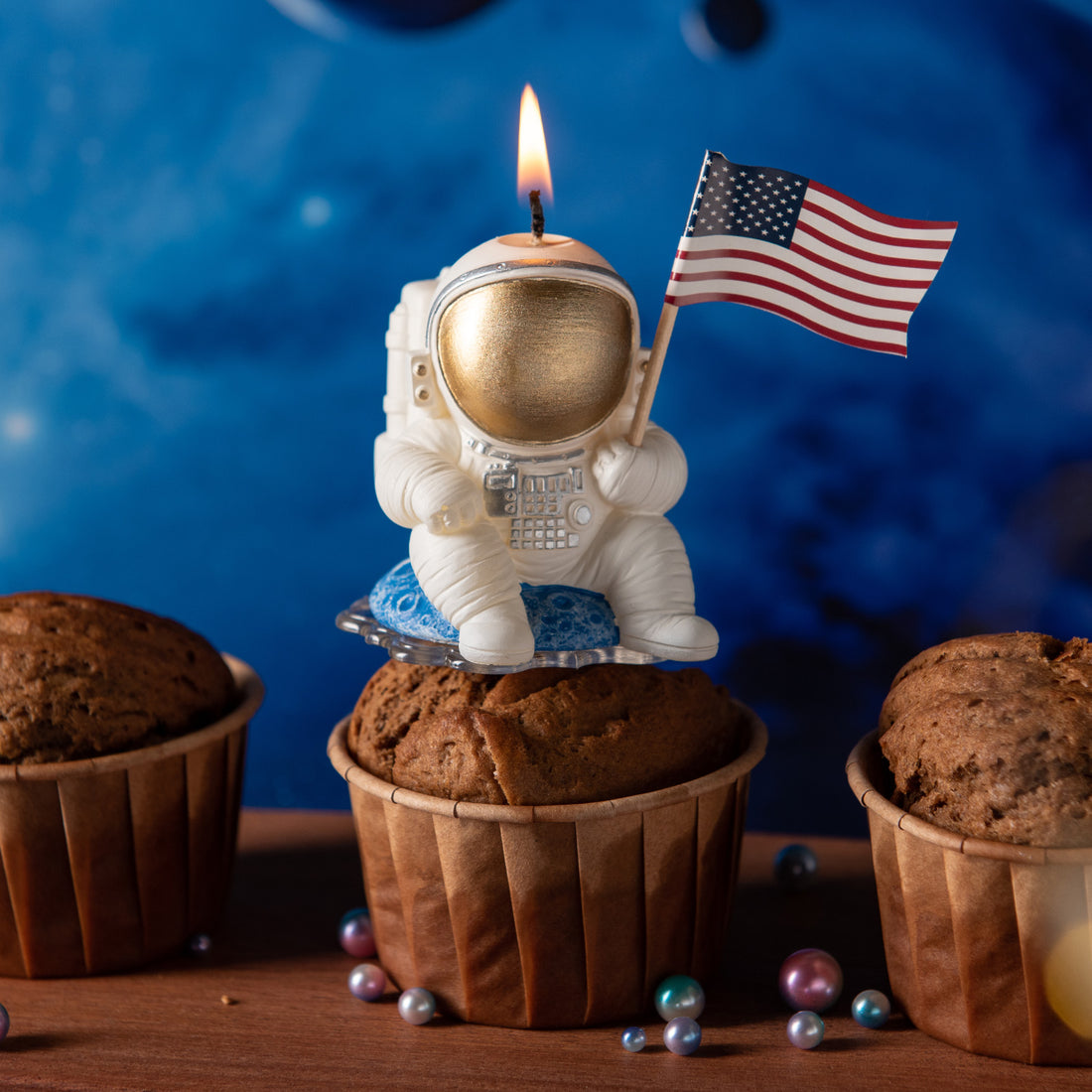 Southlake Gifts Astronaut Landing Candle lit atop a cupcake, featuring an astronaut holding a U.S. flag while seated on a blue planet, a handmade space-themed cake topper candle and imaginative gift for birthday celebrations.
