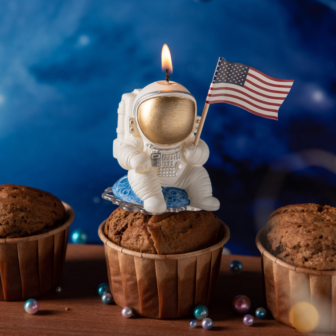 Southlake Gifts Astronaut Landing Candle lit on a cupcake, featuring an astronaut holding a U.S. flag seated on a blue planet, a handmade space-themed cake topper candle perfect for birthday celebrations.