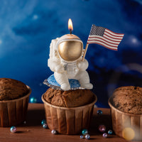 Southlake Gifts Astronaut Landing Candle lit on a cupcake, featuring an astronaut holding a U.S. flag seated on a blue planet, a handmade space-themed cake topper candle perfect for birthday celebrations.