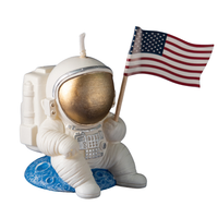 Side angle of Southlake Gifts Astronaut Landing Candle featuring an astronaut holding a U.S. flag while seated on a blue planet in a white back ground. 