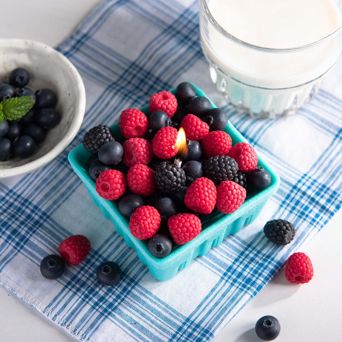 A close-up of the Southlake Gifts Berry Basket Candle lit and glowing, filled with realistic wax blueberries, raspberries, and blackberries in a handmade teal wax basket — an artisan handmade candle that makes a thoughtful gift for any season.