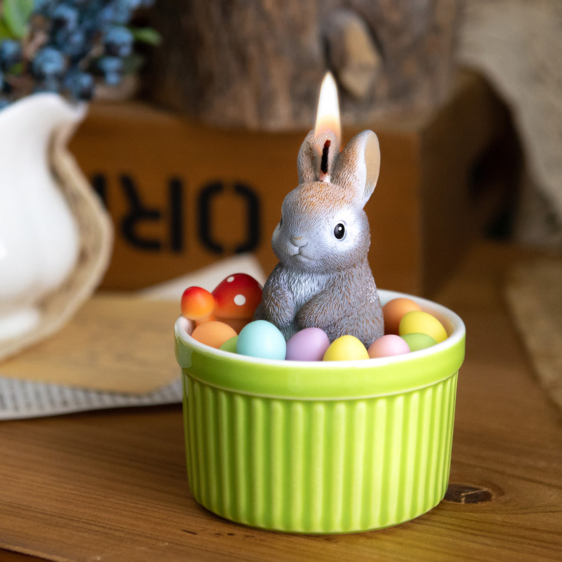 Southlake Gifts Bunny Easter Candle Bowl lit on a wooden table, featuring a gray bunny surrounded by pastel wax eggs in a green ceramic bowl, a handmade Easter décor candle perfect as a seasonal spring gift.