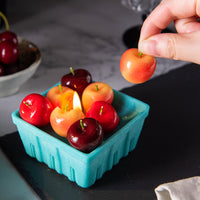 Hand lifting a Rainier cherry wax melt from the Southlake Gifts Cherry Basket Candle, showing removable wicked fruit candles for cake toppers, party décor, and creative gifting.