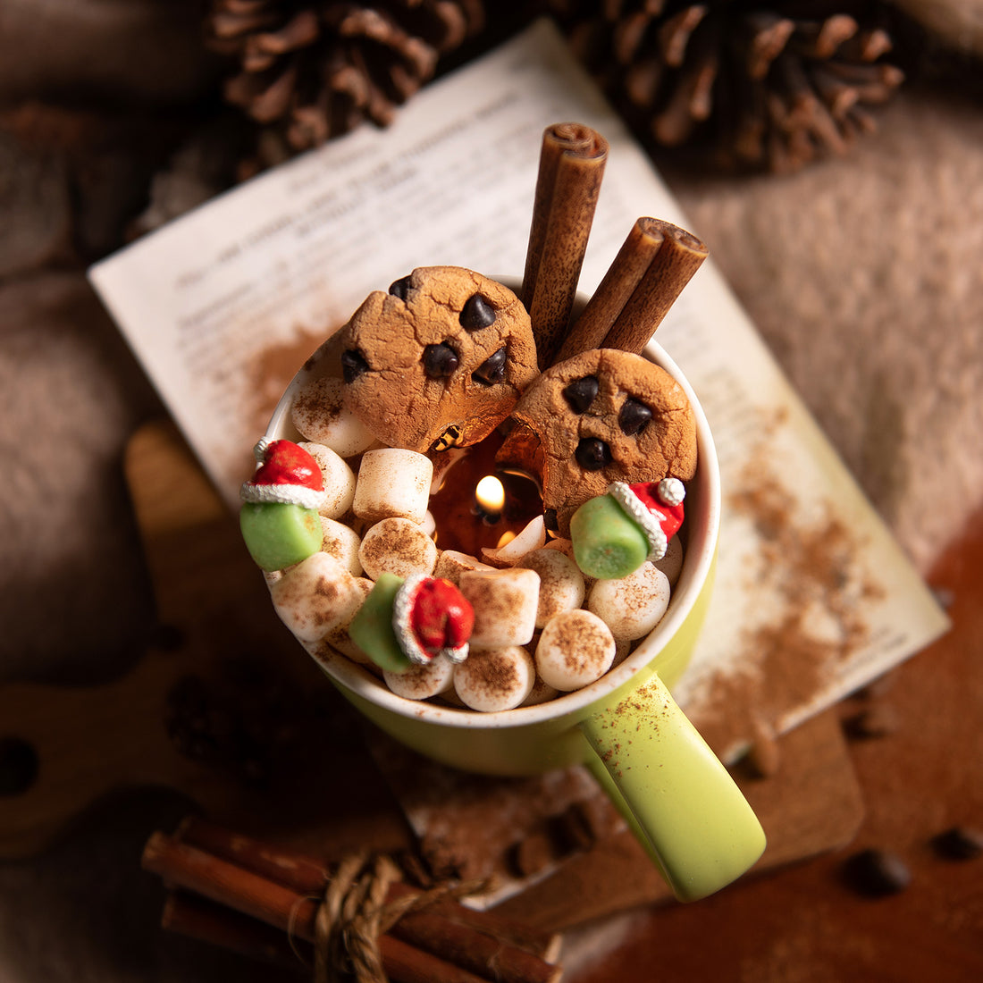 Top view of Fireside Cocoa Candle Mug by Southlake Gifts showing detailed soy wax chocolate chip cookies, green marshmallow Santa hats, and dusted cinnamon décor for cozy winter vibes and unique holiday gifts. 