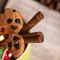 Close up look at the Cinnamon sticks candle wax melt and Chocolate Chip cookies wax melts sitting inside the  holiday cocoa candle mug — handcrafted by Southlake Gifts for realistic food candle. 