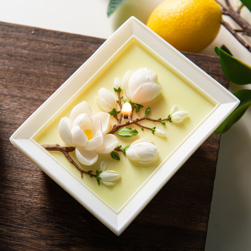 Handcrafted framed magnolia candle by Southlake Gifts shown lying flat while lit, highlighting sculpted magnolia blossoms and branches inside a picture-frame candle design, a botanical scented candle that makes a beautiful artisan gift for home styling lovers.
