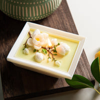 Close-up of Southlake Gifts Framed Magnolia Bloom Candle laid flat, revealing layered magnolia petals and branches embedded in soy wax, a botanical art candle designed as decorative home décor and an elevated gift for special occasions.