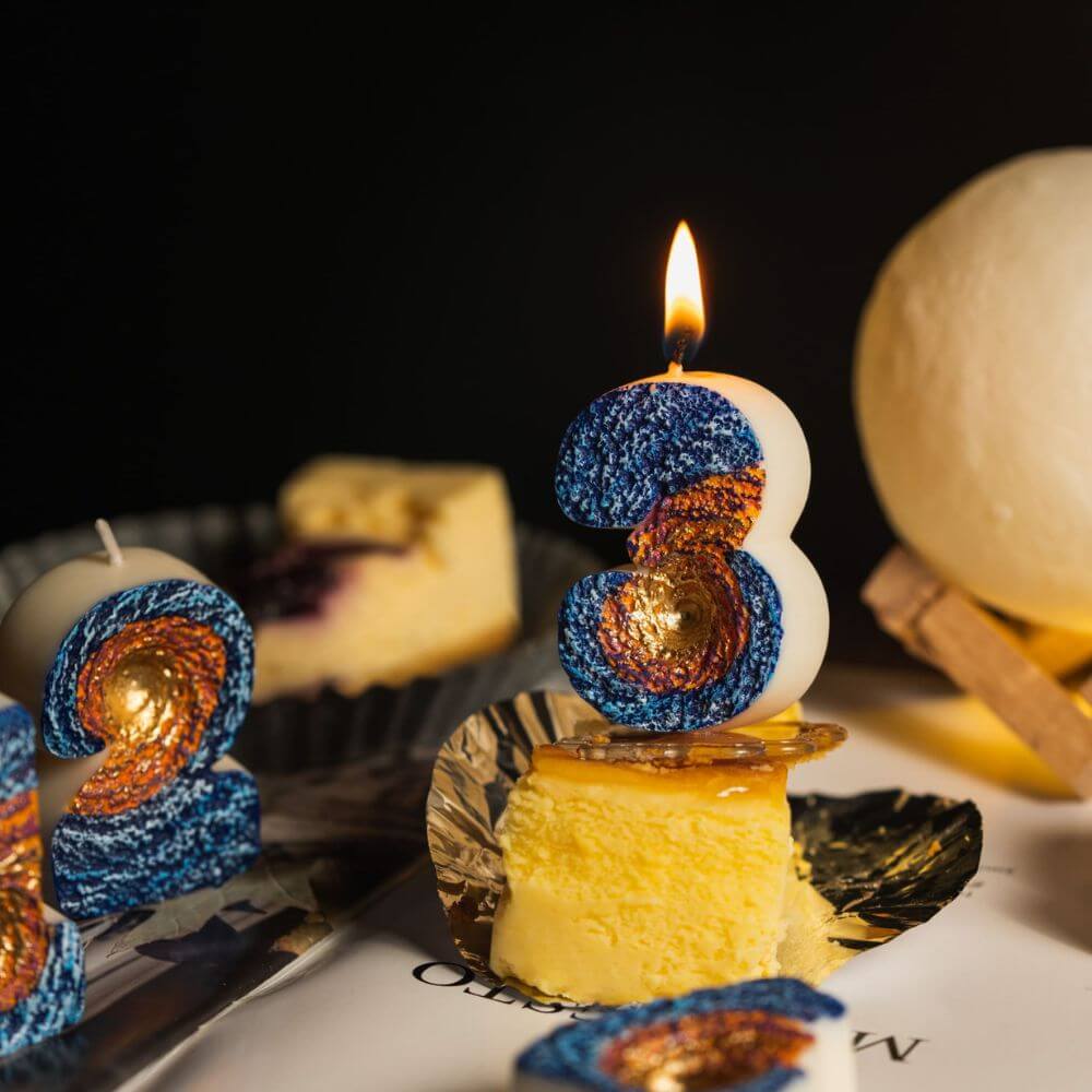 Southlake Gifts Galaxy black hole number candles displayed around cheesecake dessert with a lit number 3 candle as a birthday cake topper, space themed novelty candles for a cosmic celebration.