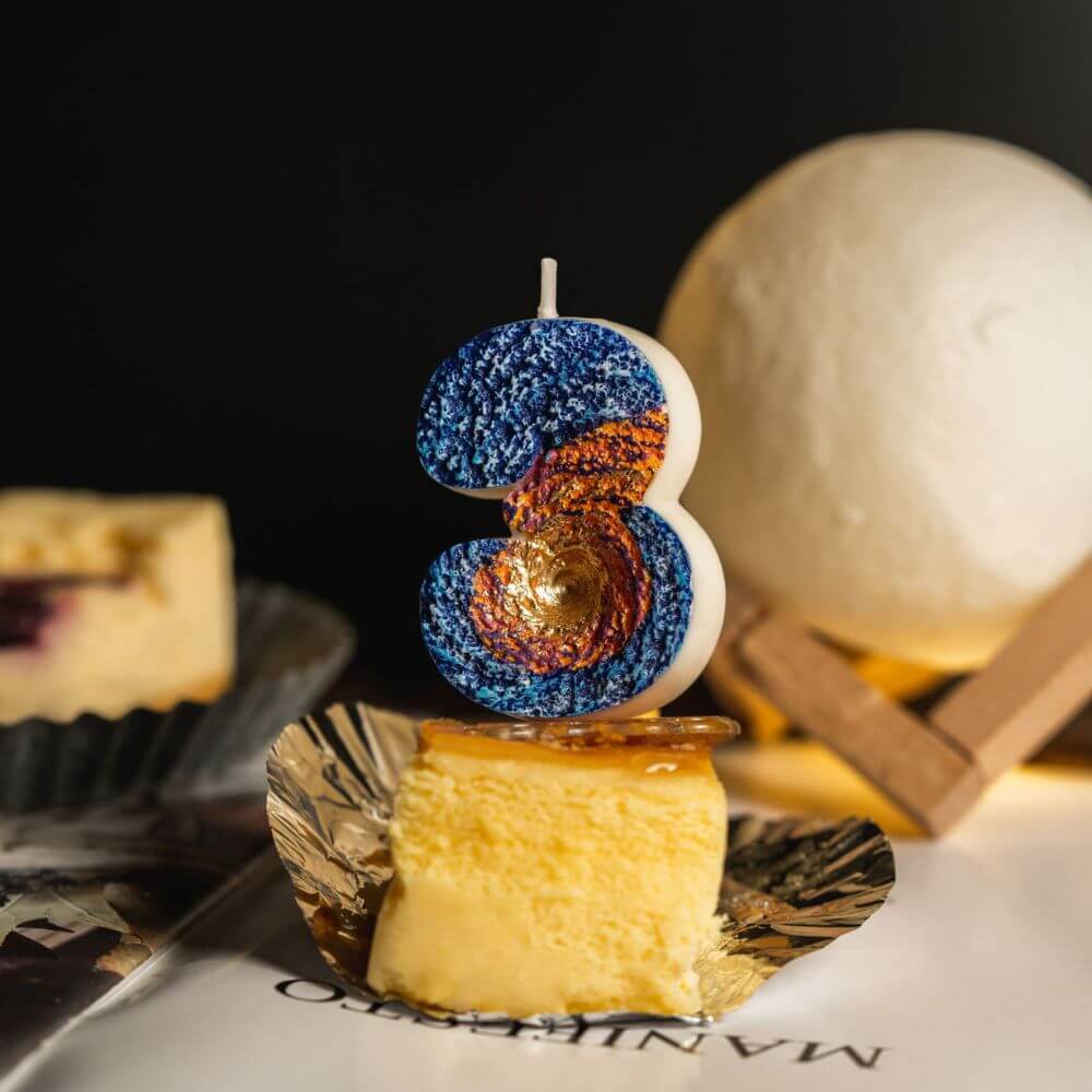 Southlake Gifts Galaxy black hole number 3 candle styled on cheesecake dessert with moon lamp background, a cosmic themed birthday cake topper and space novelty candle.