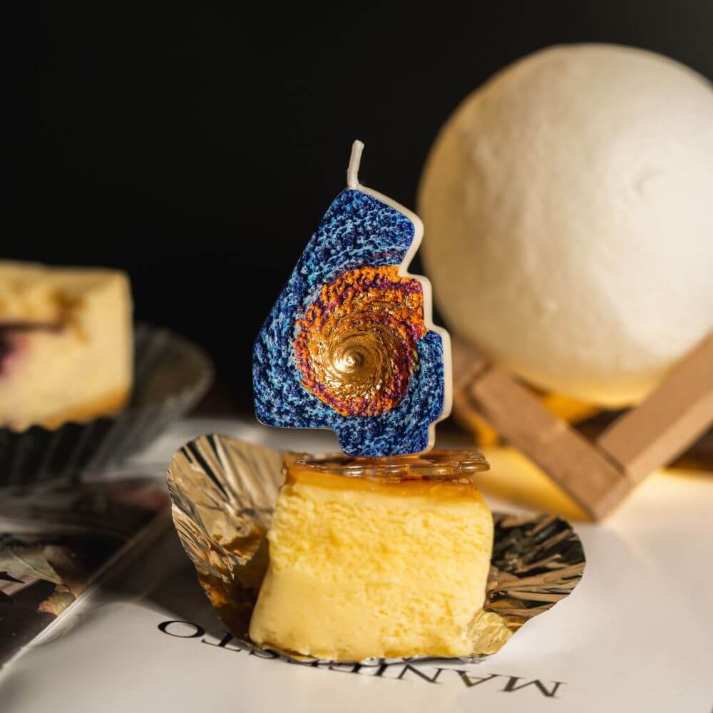 Southlake Gifts Galaxy black hole number 4 candle placed on cheesecake slice with moon lamp decor, a handmade space themed birthday candle and cake topper.