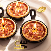 Southlake Gifts Heart Pepperoni Mini Pizza Candle Trio lit on a decorative plate, featuring realistic miniature pizzas with heart-shaped pepperoni in black skillets, a handmade novelty food candle set that makes a perfect holiday gift for pizza lovers and home candle décor fans