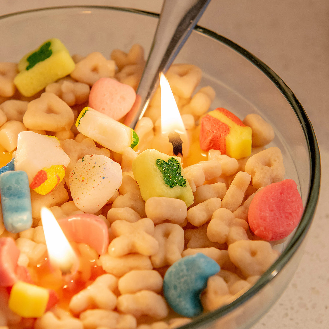 Close-up of the Lucky Charms Cereal Candle 2.0 burning, showing colorful marshmallow wax shapes like rainbows, hearts, and stars — a detailed novelty candle that makes a magical artisan gift.