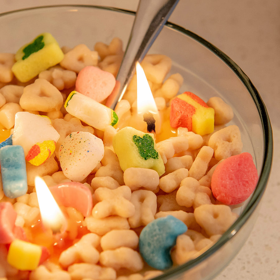 Close-up of the Lucky Charms Cereal Candle 2.0 burning, showing colorful marshmallow wax shapes like rainbows, hearts, and stars — a detailed novelty candle that makes a magical artisan gift.