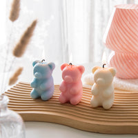 Southlake Gifts Mysterious Gummy Bear Candle shown in three color variants—white, pink, and blue—lit on a wooden board, a handmade scented novelty candle gift with a hidden heart inside.