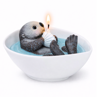 The back view of the cute Southlake Gifts sea otter animal candle is lit up in the white background. 