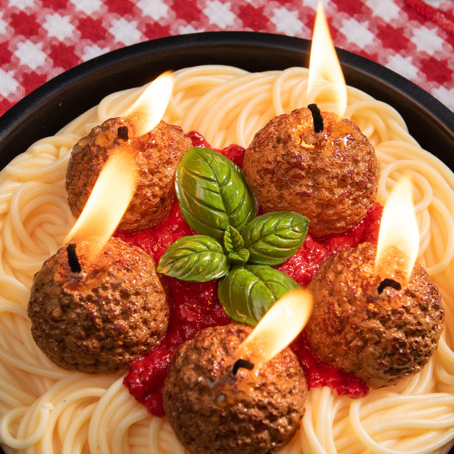 Southlake Gifts Spaghetti and Meatballs Candle with wax basil leaves and tomato sauce, lit and displayed in a black bowl on a red checkered tablecloth — a hyper-realistic handmade pasta candle that makes a fun and thoughtful gift for food lovers and home décor fans.