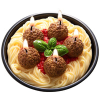 Southlake Gifts Spaghetti with meatballs candle, and shaped like basil leaves, plus tomato sauce sitting on a pen and lit on a black reusable pan in a white background