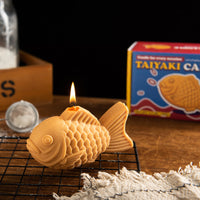 Southlake Gifts taiyaki candle on cooling rack with lit flame, realistic Japanese dessert food candle with detailed texture, novelty candle gift for Japanese food lovers, unique foodie gift, kawaii decor and playful home decoration