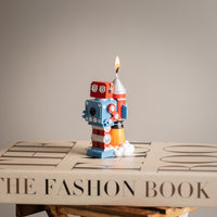 Southlake Gifts Vintage Robot Rocket Candle displayed on a fashion book, featuring a hand-painted retro robot with rocket flame — an artisan handmade candle that makes a thoughtful gift for any season.
