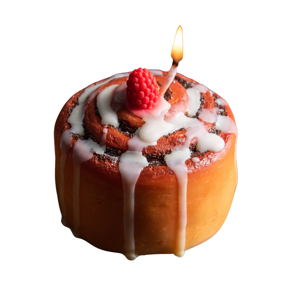 Cinnamon pastry dessert food candle with frosted wax drizzle and raspberry topper is lit up in white background – handmade soy wax food candle for cozy décor.
