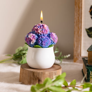 Southlake Gifts Hydrangea Candle lit in a white ceramic pot, showcasing hand-painted purple and blue petals with lifelike floral texture — a handmade scented candle that makes a thoughtful gift for home décor lovers.