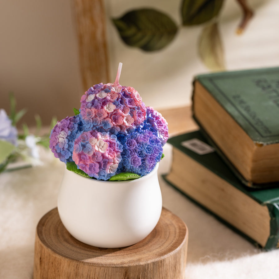 Unlit Hydrangea Candle displayed beside vintage books and greenery, featuring delicate violet and lilac hues — an artisan floral candle ideal for gifting during spring or Mother’s Day.