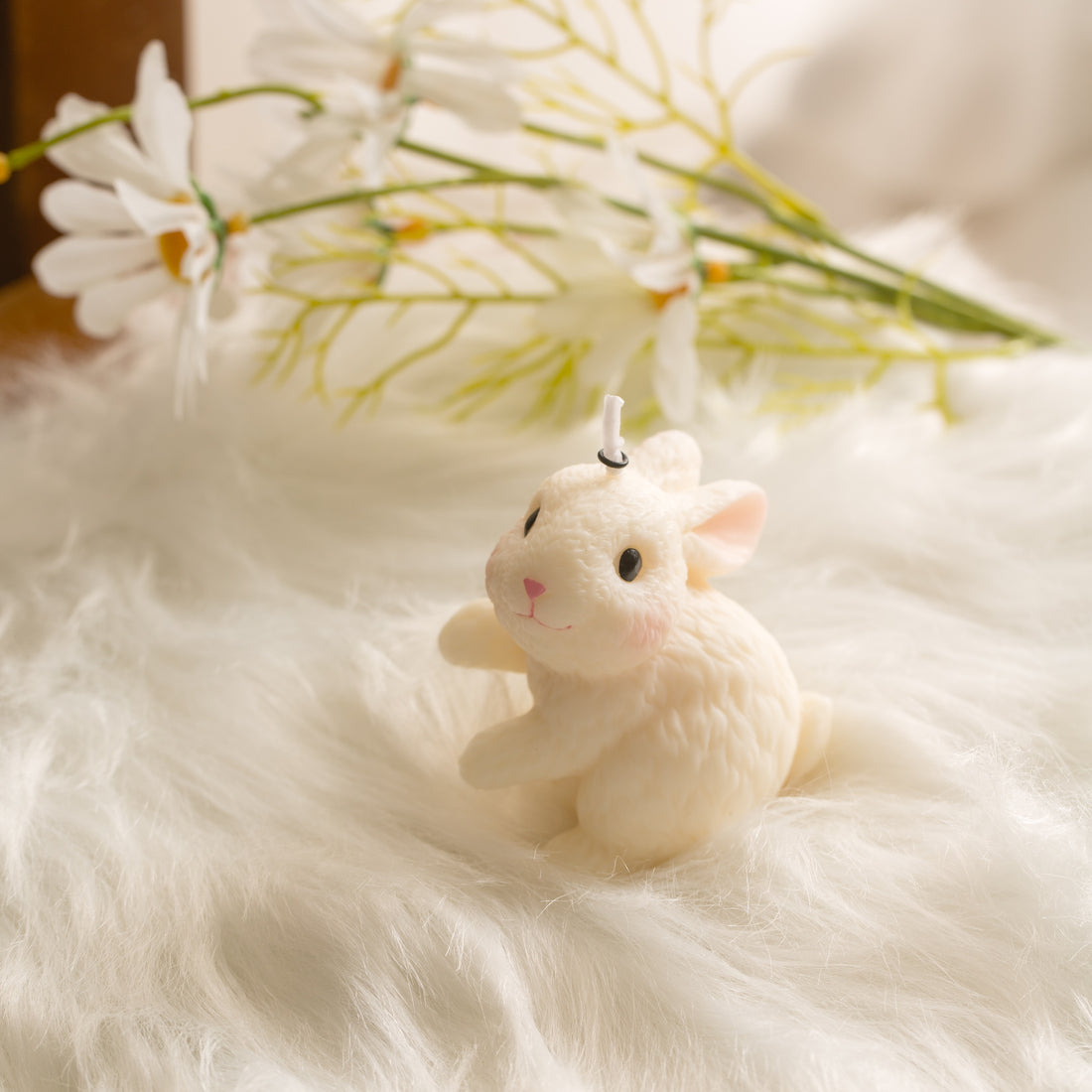 Blushing Bunny Candle Looking Left resting on soft white fur with spring daisies, unscented handmade rabbit candle perfect for Easter table decor and cake topper gift