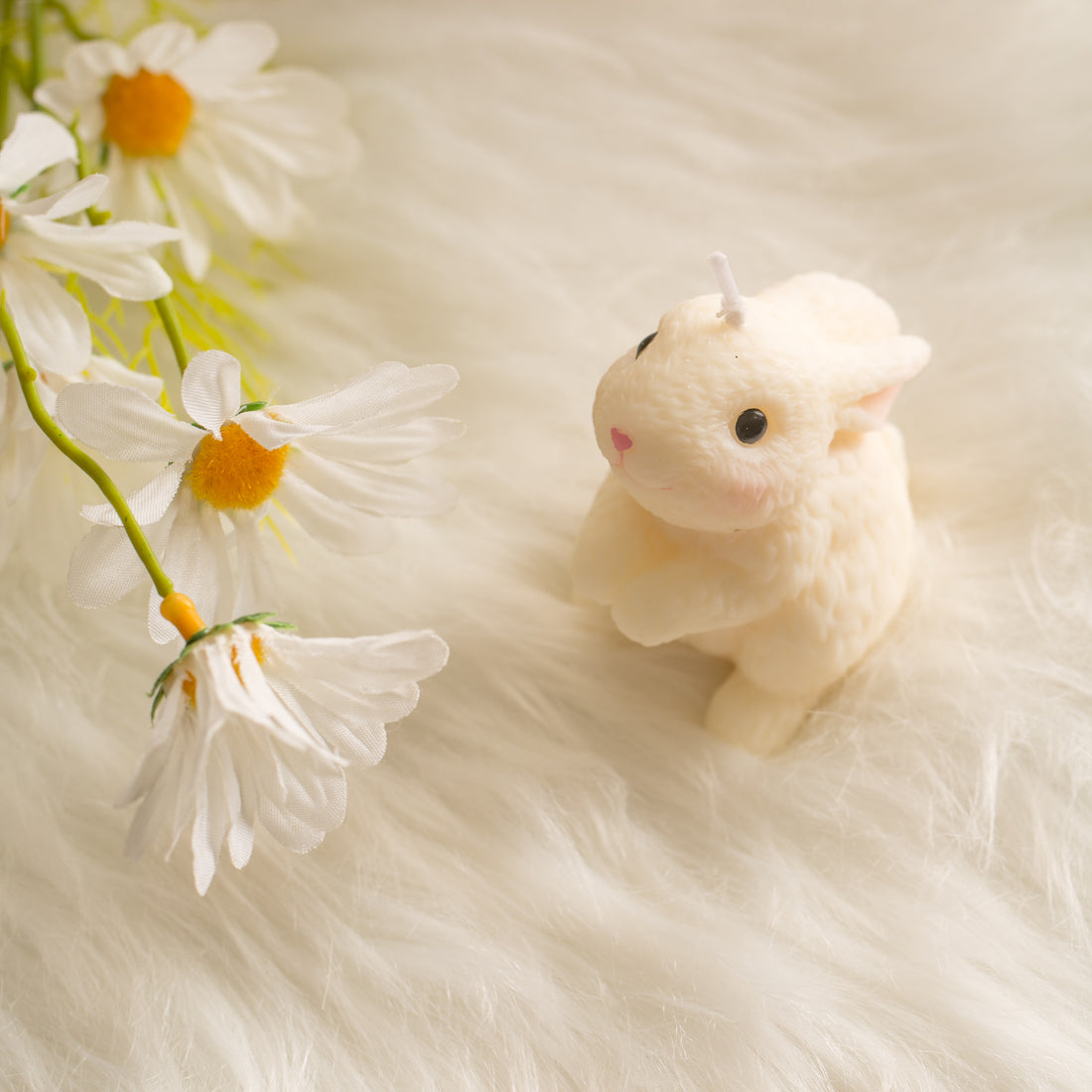 Blushing Bunny Looking Up rabbit candle beside spring daisies on soft faux fur, unscented Easter decor accent for brunch tables and seasonal styling. 