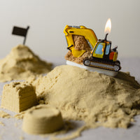 Lit Southlake Gifts Excavator Candle sitting on sand, a realistic construction-themed candle cake topper that brings playful charm to birthday cakes and party décor.