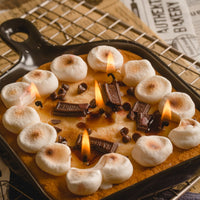 Lit Skillet S’more Candle on cooling rack — artisan soy wax candle shaped like a baked s’more, a thoughtful handmade gift for chocolate lovers and cozy home décor.